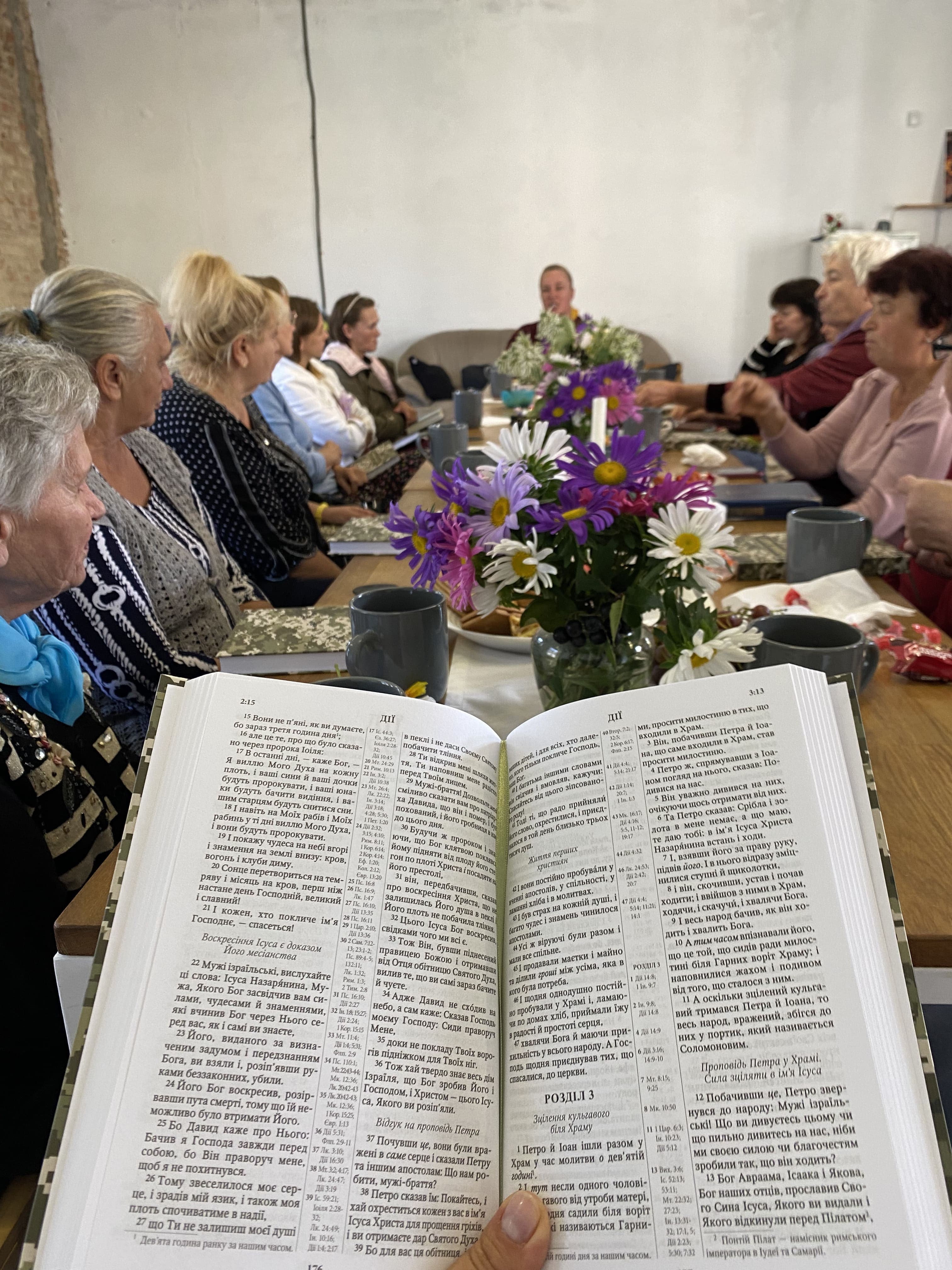 Людина тримає біблію. На фоні люди сидять за столом