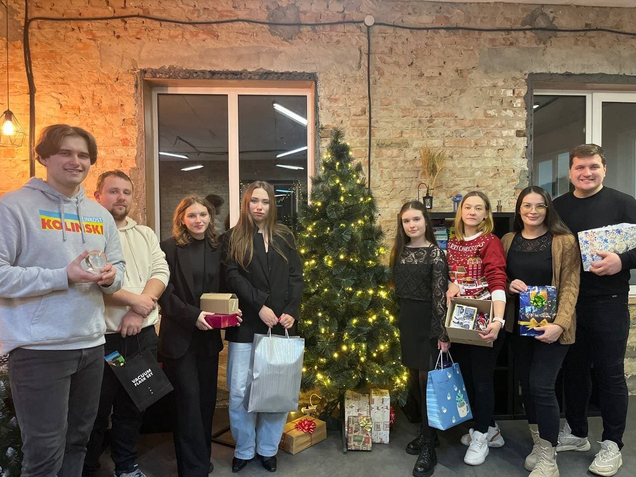 Група молоді на фоні різдвяної ялинки тримає подарунки та посміхається